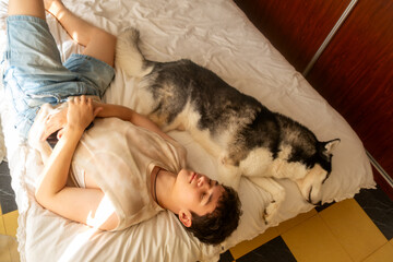 A 17-year-old teenage boy lies with a husky dog ​​in bed, the concept of friendship and comfort