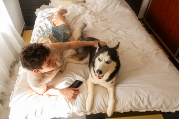 teenage boy lies with a husky dog ​​in bed, the concept of friendship and comfort