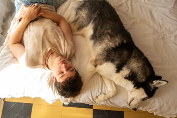 A 17-year-old teenage boy lies with a husky dog ​​in bed, the concept comfort
