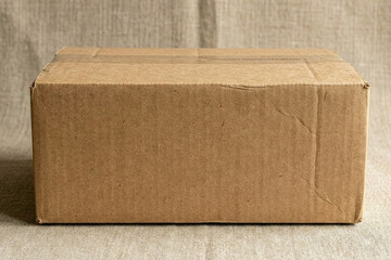 Front view of a closed brown cardboard shipping box sealed with tape on a textured linen background