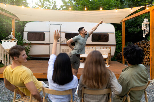 Diverse young friends playing charades near camper van, trying to guess word during outdoor party. Millennial people entertaining themselves with guessing game, having fun camping trip