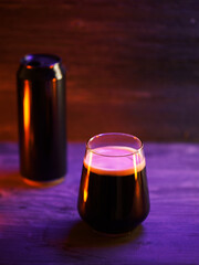 Craft dark stout beer in a glass on a wooden table. Creamy beer foam. Beer can