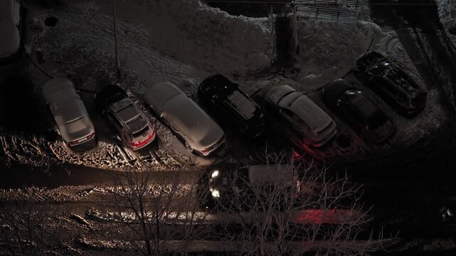 Description (Adobe optimized):
Top-down view of cars moving along a snow-covered road at night, with parked vehicles lining the street. Cold winter atmosphere captures urban traffic and everyday city 
