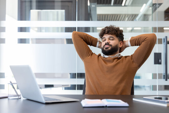 Young professional leaning back in his office chair with eyes closed, taking a calm, restorative break to relieve stress and refocus in a modern workplace setting