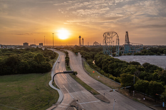 Aerial Drone View of Rollercoaster Rides Near Busy Highway Roads With Bright Orange Sun At Dusk Sunset