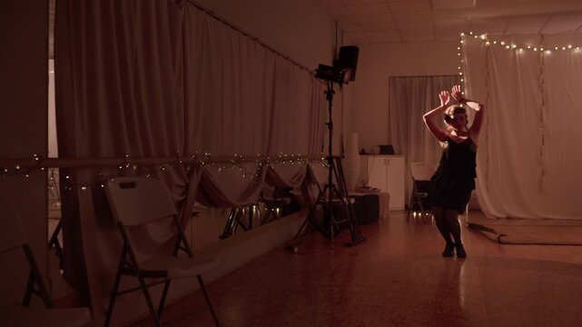 Sexy woman in retro attire with fancy vintage hairstyle dancing alone in low-light hall, performing elegant dance movements with cheerful expressive energy, classic nostalgic style captured. 4K video