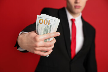 Businessman in suit showing dollar banknotes on red background, closeup
