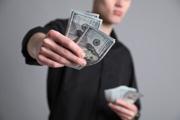 Businessman giving dollar banknotes on grey background, closeup