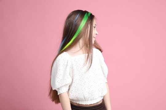 Cute girl with bright clip-in hair extensions on pink background