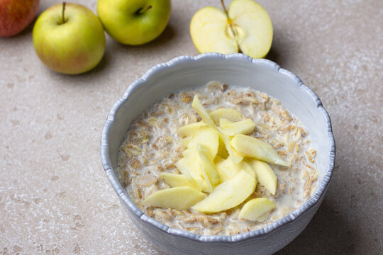 Multigrain cereal porridge made from rye, oats, barley, buckwheat and wheat flakes, served with milk and fresh apple slices. Neutral stone background, soft daylight, healthy breakfast concept