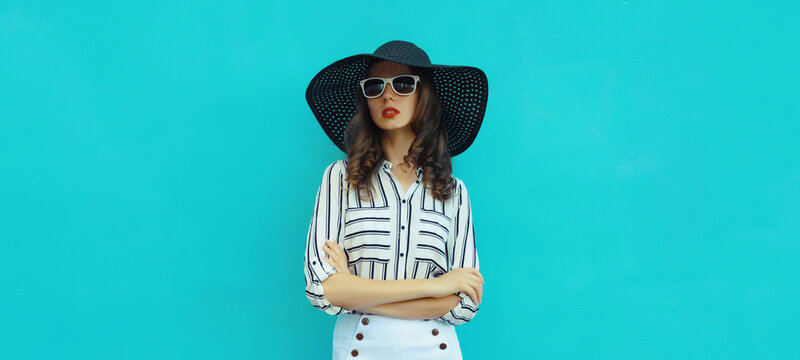 Beautiful stylish young woman in summer black straw hat against blue wall background