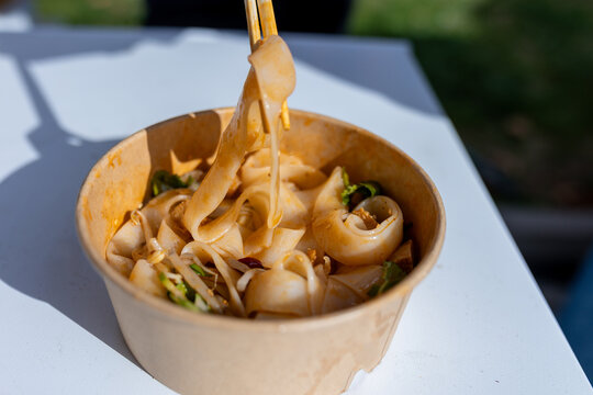Close-up of a person eating authentic Liangpi Chinese noodles with chopsticks at an outdoor street market