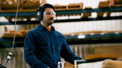 Male woodworker wearing ear protection and safety goggles, focusing on operating woodworking machinery in a professional workshop