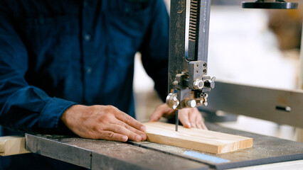 Skilled carpenter pushing a wooden board through a bandsaw, shaping material in a workshop, focusing on craftsmanship