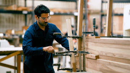 Male carpenter in a workshop clamping pieces of wood together, focusing on precision and...