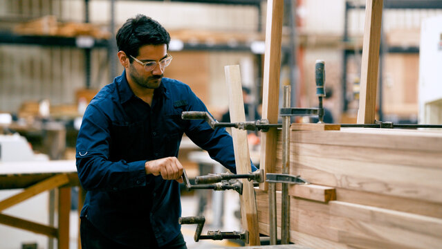 Male carpenter in a workshop clamping pieces of wood together, focusing on precision and craftsmanship