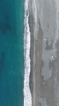 Vertical drone footage of a sandy coastline with winter waves crashing on the beaches enhancing the contrast between the blue sea and white wave lines 2