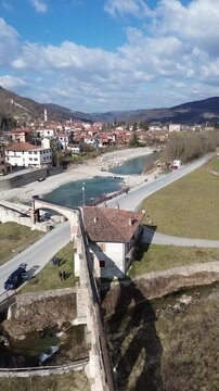Cinematic vertical drone footage of Tanaro River with ancient Roman bridge and Bagnasco city on the left bank and old mill on the right bank captured on a sunny winter day 3