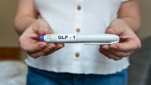 GLP-1 injection pen held by woman in front of abdomen, weight management concept