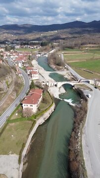 Cinematic vertical drone footage of Tanaro River with ancient Roman bridge and Bagnasco city on the left bank and old mill on the right bank captured on a sunny winter day 2