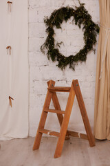 Wooden ladder beside decorative wreath on white brick wall indoors