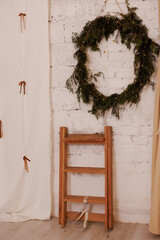 Wooden ladder beside wreath decoration on white brick wall indoors