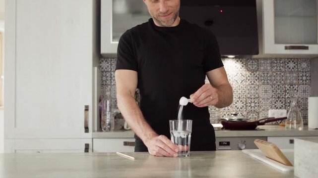 4K close-up fit male preparing protein shake in kitchen. Pouring creatine powder into glass for muscle growth. Healthy nutrition, fitness lifestyle, sport training and bodybuilding concept