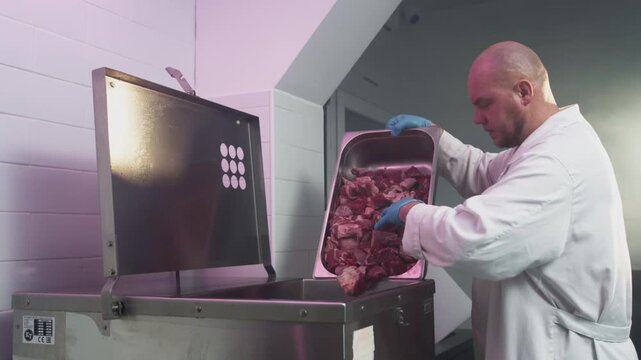 Man worker in white robe empties minced meat from a large metal basin. Processing of production ground beef in industrial grinder. Make keema or qeema. Food industry, ground beef preparation.