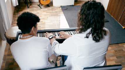 Music teacher guiding a student's hands on an electronic piano keyboard during a lesson in a home studio