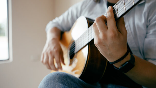 Musician hands strumming and fretting chords on an acoustic guitar. Creating music with a string instrument. Hobby and passion - Powered by Adobe