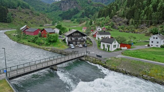 Aerial view of bridge and houses along the river in Flam, Norway. Drone footage shows village buildings, flowing water and green mountain valley.