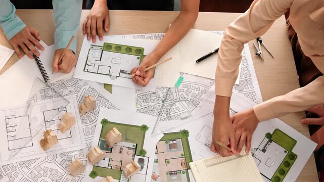 Architect and safety engineer discussion about building construction use blueprint on table with architectural document, measurement tool and wooden block scatter around at modern office. Delineation.