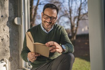Man enjoying leisure time while reading book by window