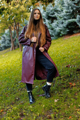 Woman in maroon coat stands on grass in park with trees in background
