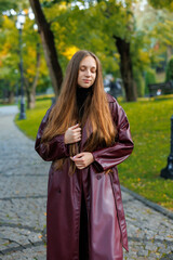 Young woman in long burgundy coat standing on stone pathway in park