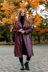 Woman in burgundy coat stands in autumn park with colorful foliage