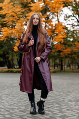 Woman in maroon coat poses outdoors among autumn foliage