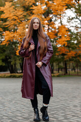Woman in burgundy coat poses outdoors among autumn foliage