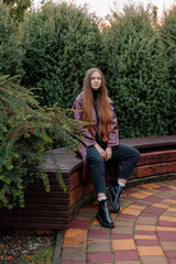 Woman with long hair sitting on a bench in a park surrounded by greenery