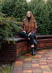 Woman with long hair sits on curved bench in garden, green foliage background