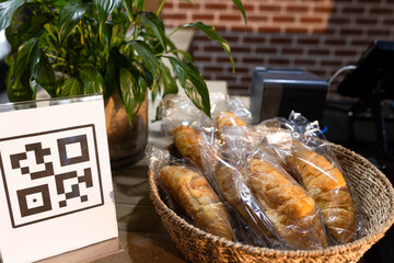 Wicker basket is holding individually wrapped pastries on cafe counter, with QR code sign nearby