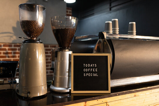 Espresso machine, 2 grinders is sitting on glossy counter, letter board TODAYS COFFEE SPECIAL, cups