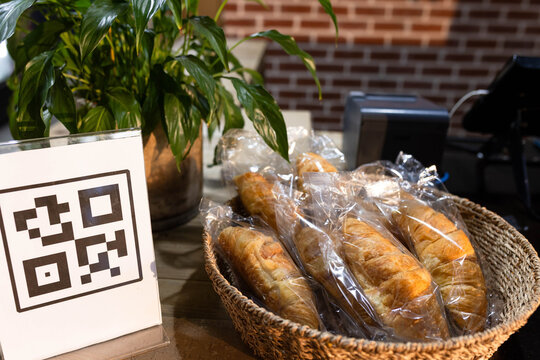 Wicker basket is holding individually wrapped pastries on cafe counter, with QR code sign nearby