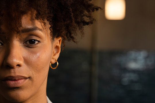 African American woman gazing at camera in warm room wearing gold hoop earring, copy space