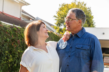 Man and senior woman standing on driveway, wearing denim, white blouse, man with eyeglasses