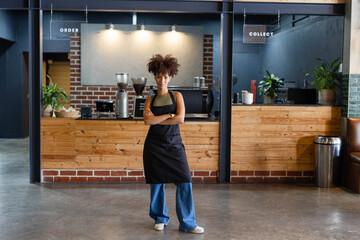 African American adult woman wearing black apron, standing in cafe by espresso machine and grinders