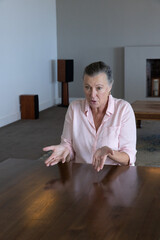 Naklejka premium Senior woman sitting at polished wooden table in living room, wearing pink shirt and gold hoops