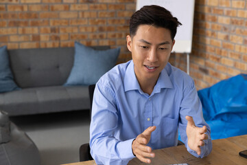 Asian man in light blue shirt gesturing while explaining at table in office lounge with keyboard