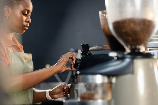 African American woman barista adjusting espresso machine holding pitcher at counter, copy space