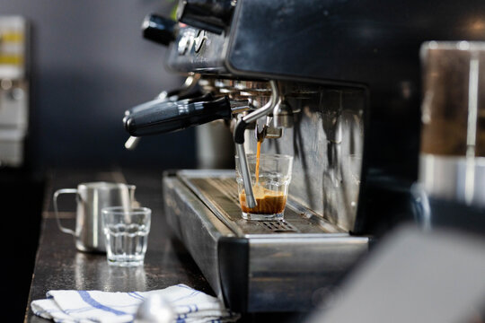 Commercial espresso machine pulling shot into clear glass on cafe counter, crema forming